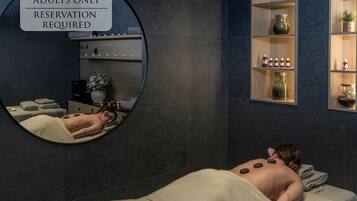 A spa area with a massage table, a mirror, and shelves with bottles and a potted plant.