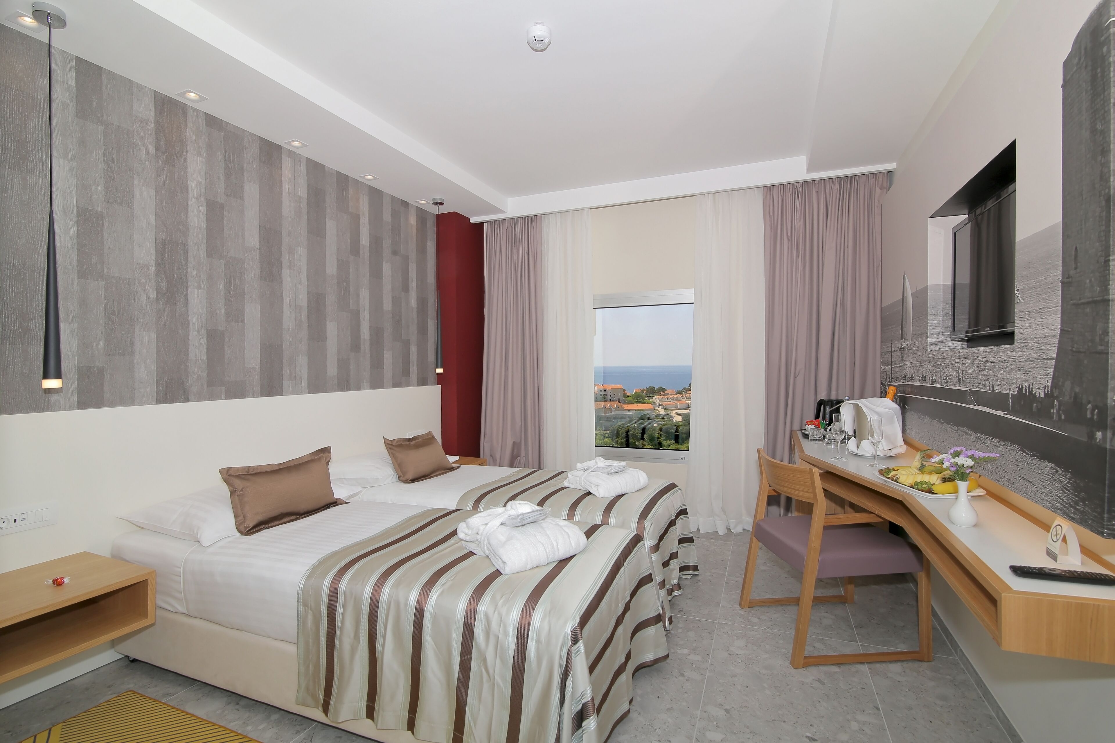 A hotel room with two beds, a desk, a chair, a window with a view, and a flat-screen TV.