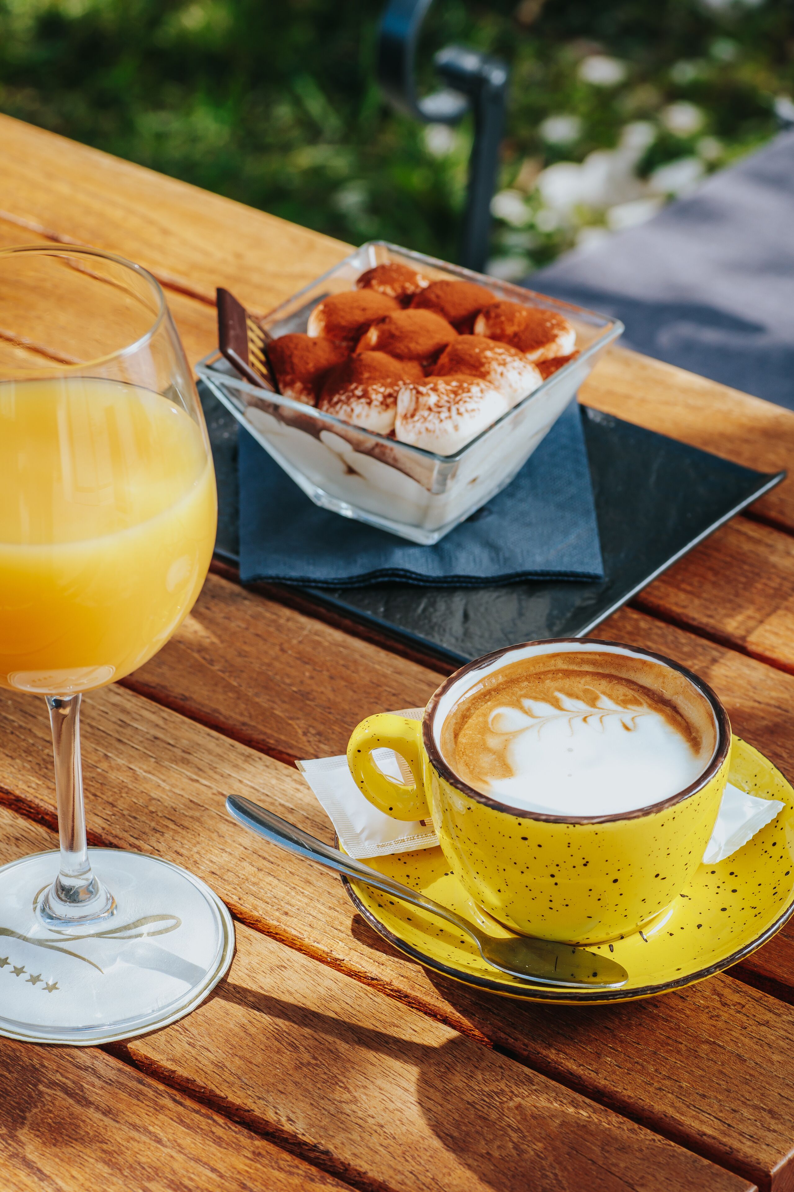 A wooden table with a glass of orange juice, a cup of coffee with latte art, and a bowl of pastries.
