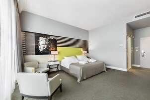 A modern hotel room with a bed, a desk, a chair, and a large artwork on the wall.