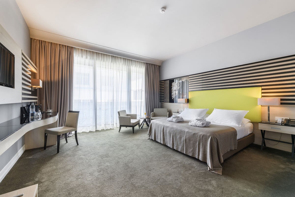 Ein modernes Hotelzimmer mit einem Bett, zwei Stühlen, einem Schreibtisch und einem Fernseher.