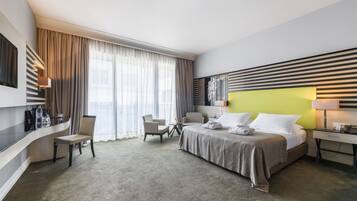 Quarto de hotel moderno com uma cama, duas cadeiras, uma escrivaninha e uma televisão.
