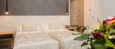 A hotel room with two beds, a desk, a chair, a large mirror, and a potted plant.