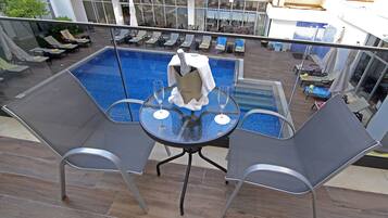 A poolside area with a glass table, two chairs, and a champagne bottle.