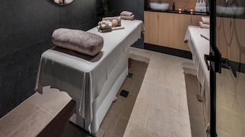 Un área de spa con una camilla de masaje, un estante pequeño con artículos de aseo y un armario de madera.