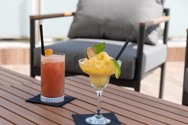 Two drinks on a wooden table with a grey cushioned chair in the background. - Hotel Lero (Dubrovnik)