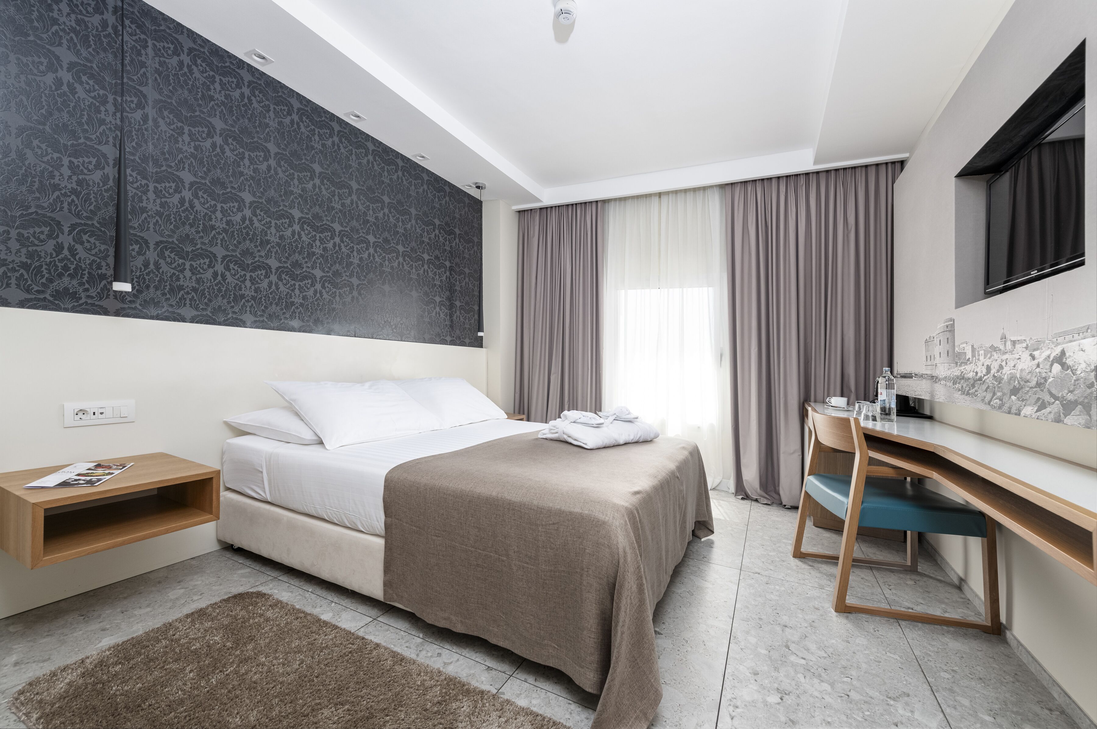 A modern hotel room with a bed, desk, and a cityscape mural on the wall.