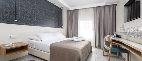 A modern hotel room with a bed, desk, and a cityscape mural on the wall.