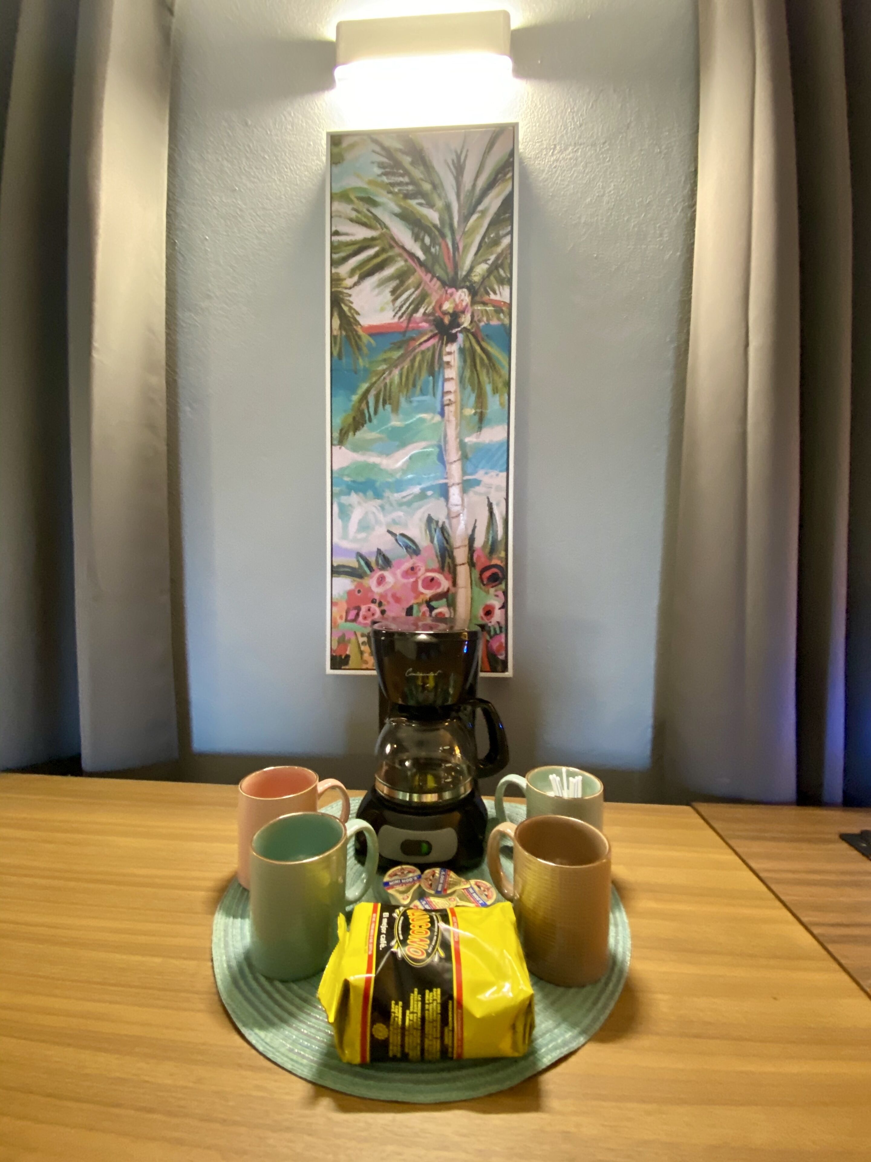 A coffee maker on a table with two mugs and a packet of snacks.