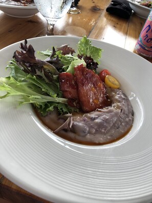 Ein weißer Teller mit Salat, Speck und Bohnen.