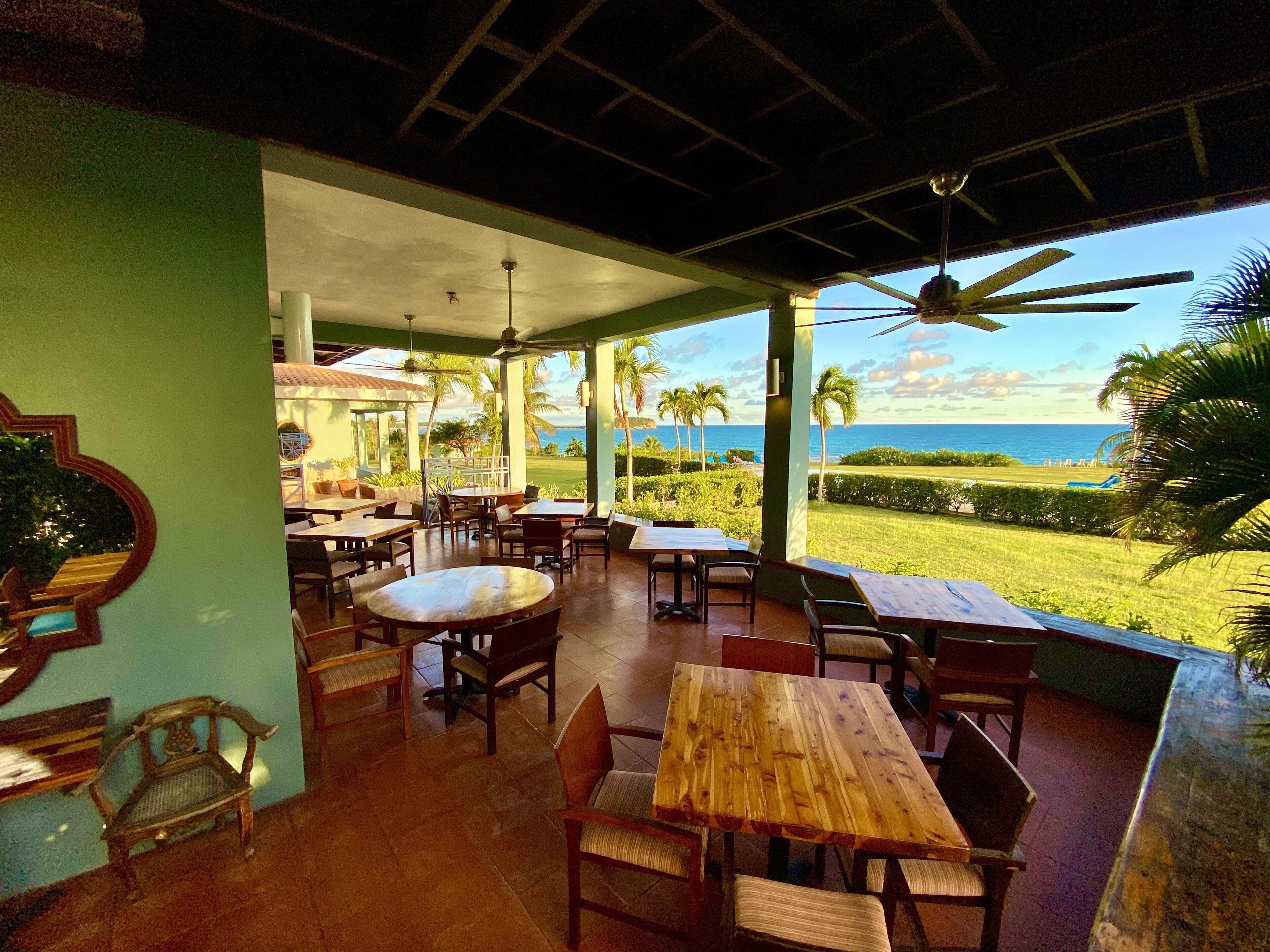 An outdoor dining area with tables and chairs, a ceiling fan, and a view of the ocean.