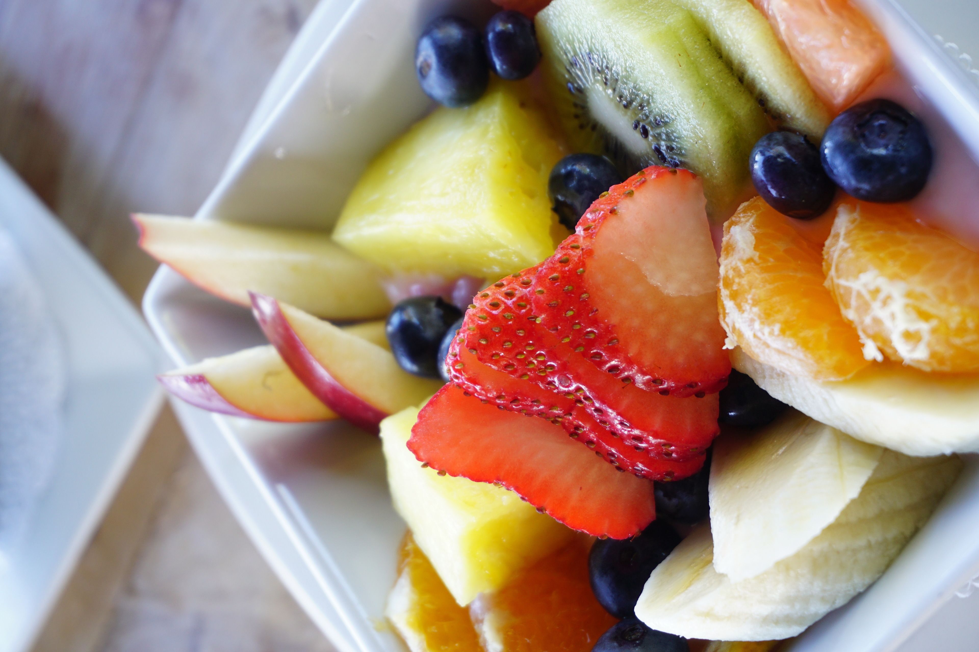 Un récipient rempli de divers fruits, notamment des fraises, des myrtilles, des kiwis et des tranches d’orange.