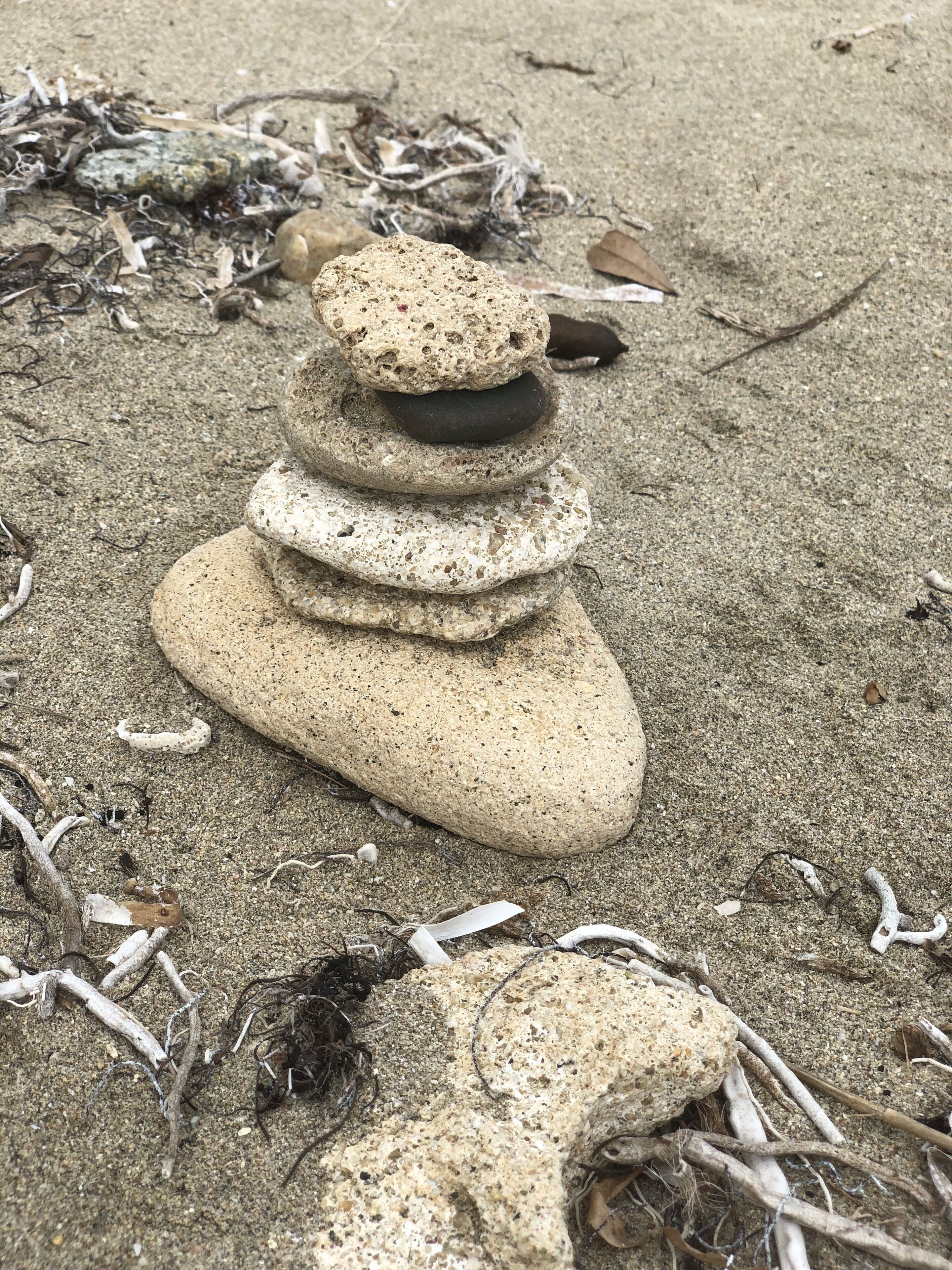 A stack of smooth, rounded stones on a sandy beach with scattered debris.