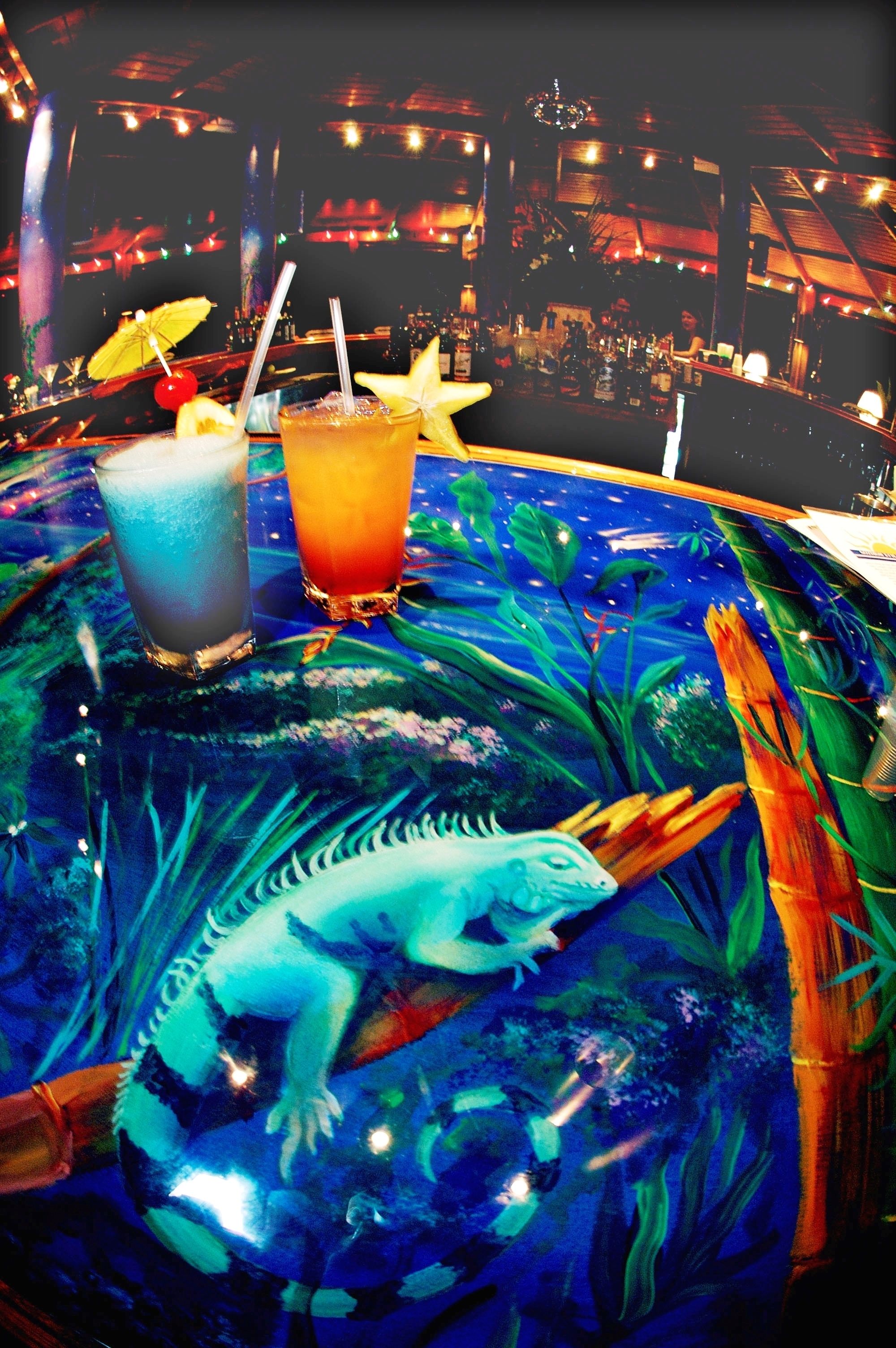 A bar area with two drinks on a table, a mural of a sea creature, and a cityscape in the background.