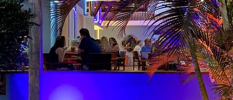 An outdoor seating area with palm trees and a blue-lit background.