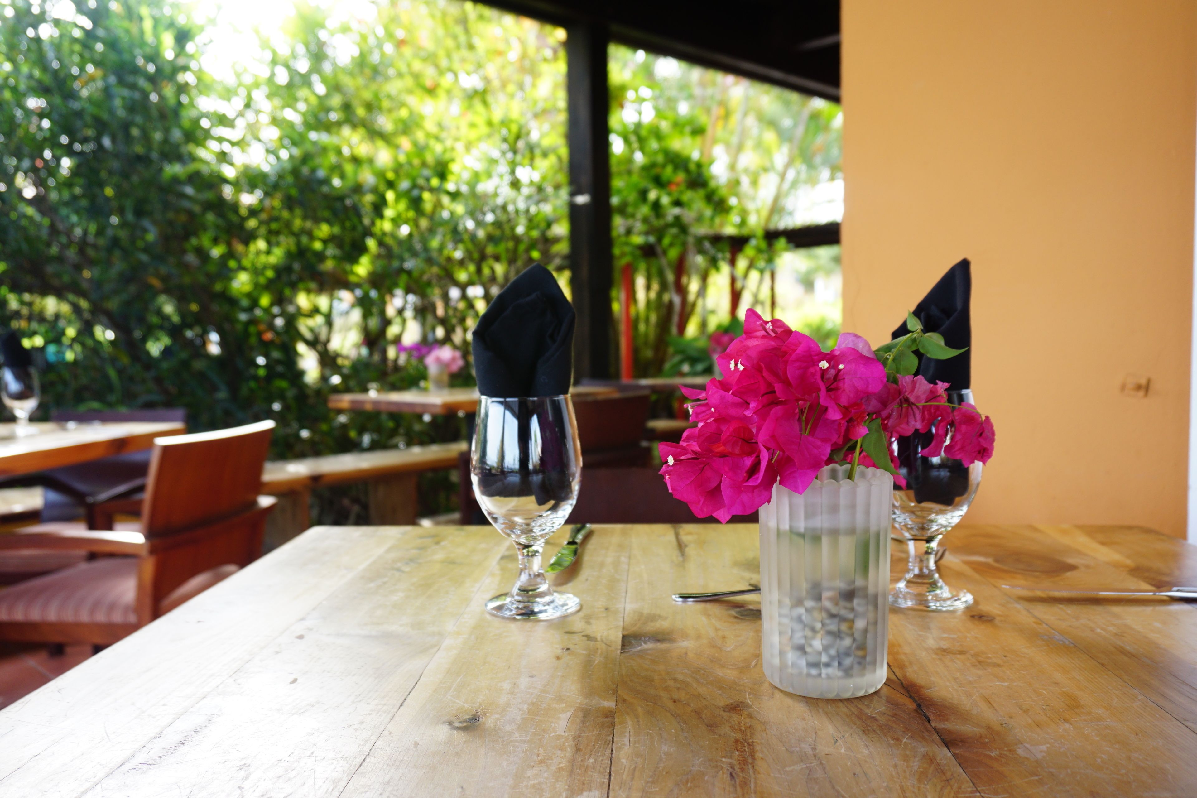 Et træbord med en glasvase med lyserøde blomster og en foldet serviet.