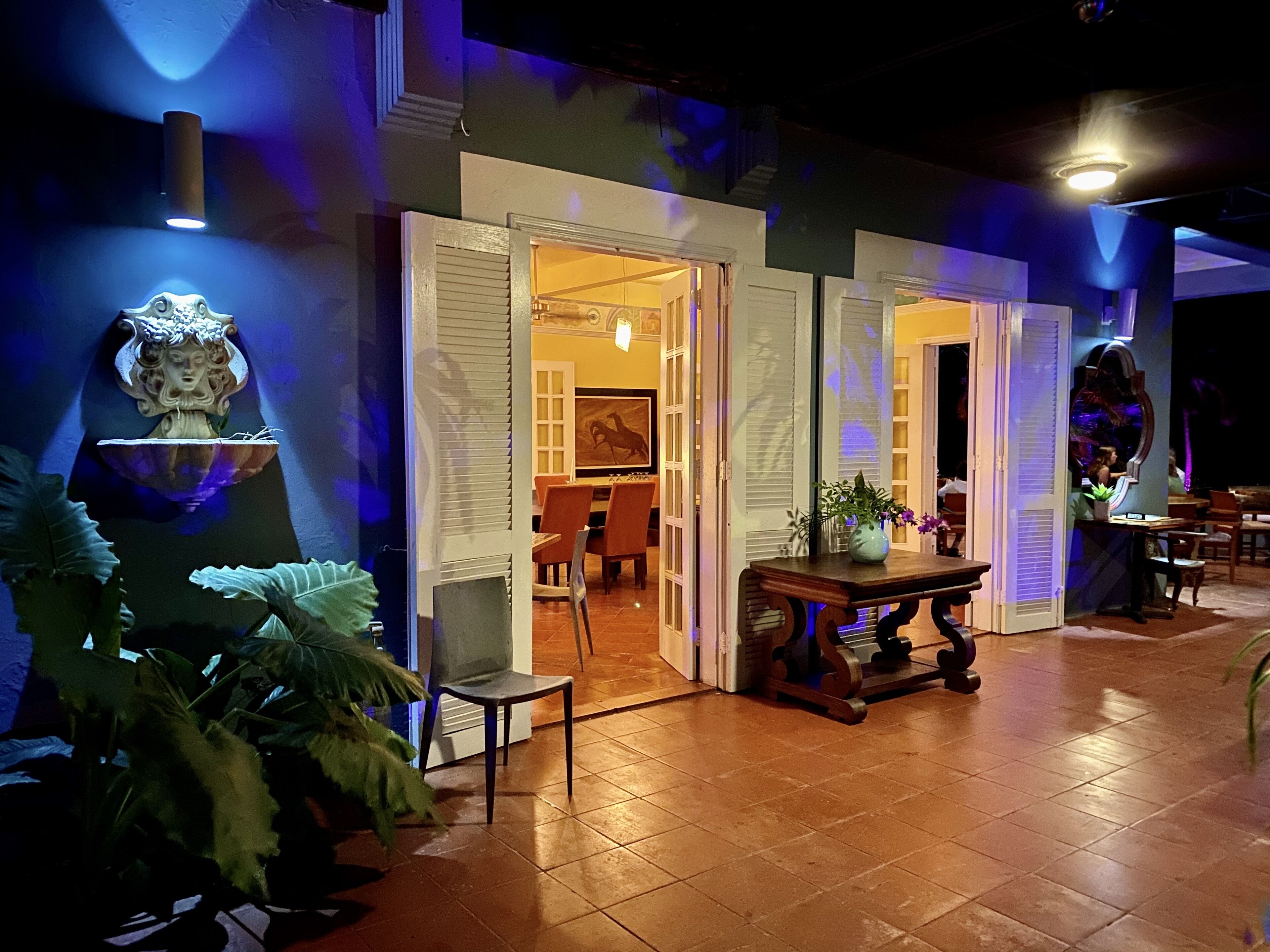 Un interior con puertas abiertas que dan a un comedor, un adorno en la pared y una mesa con un jarrón.