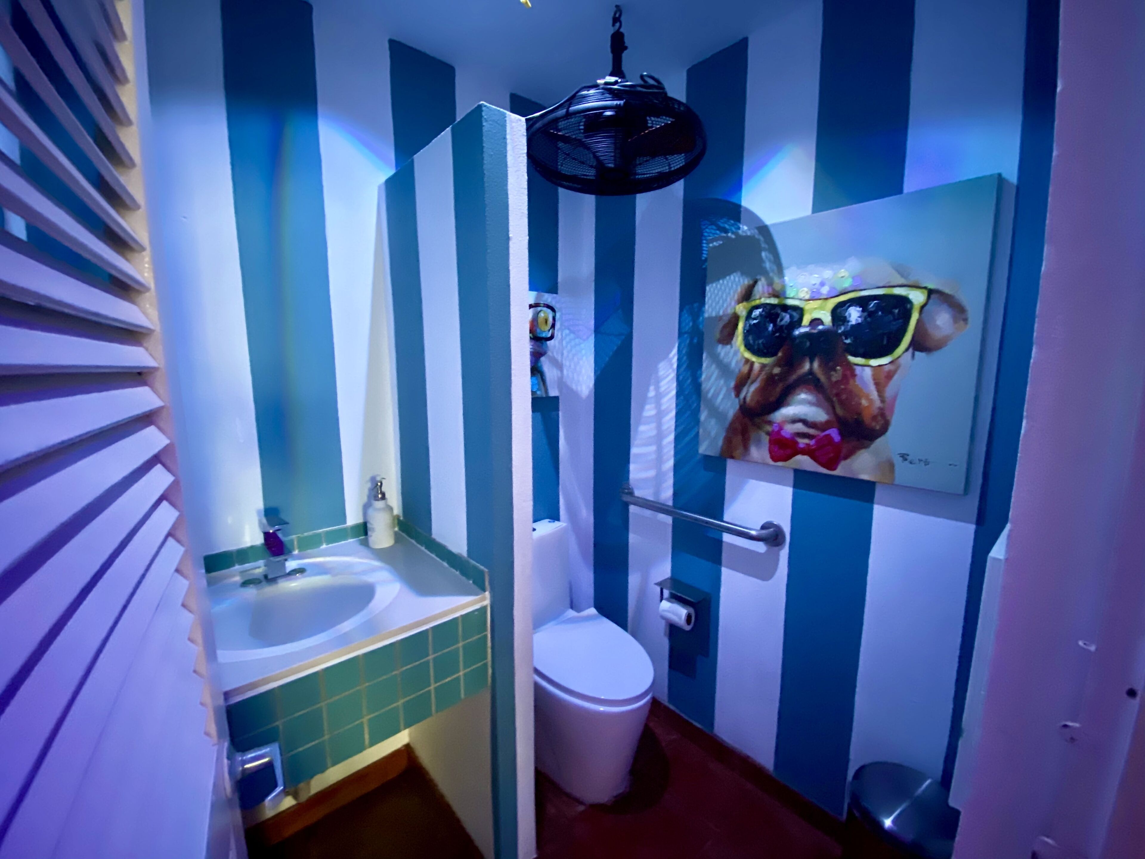 A bathroom with striped walls, a sink, toilet, and a shower.