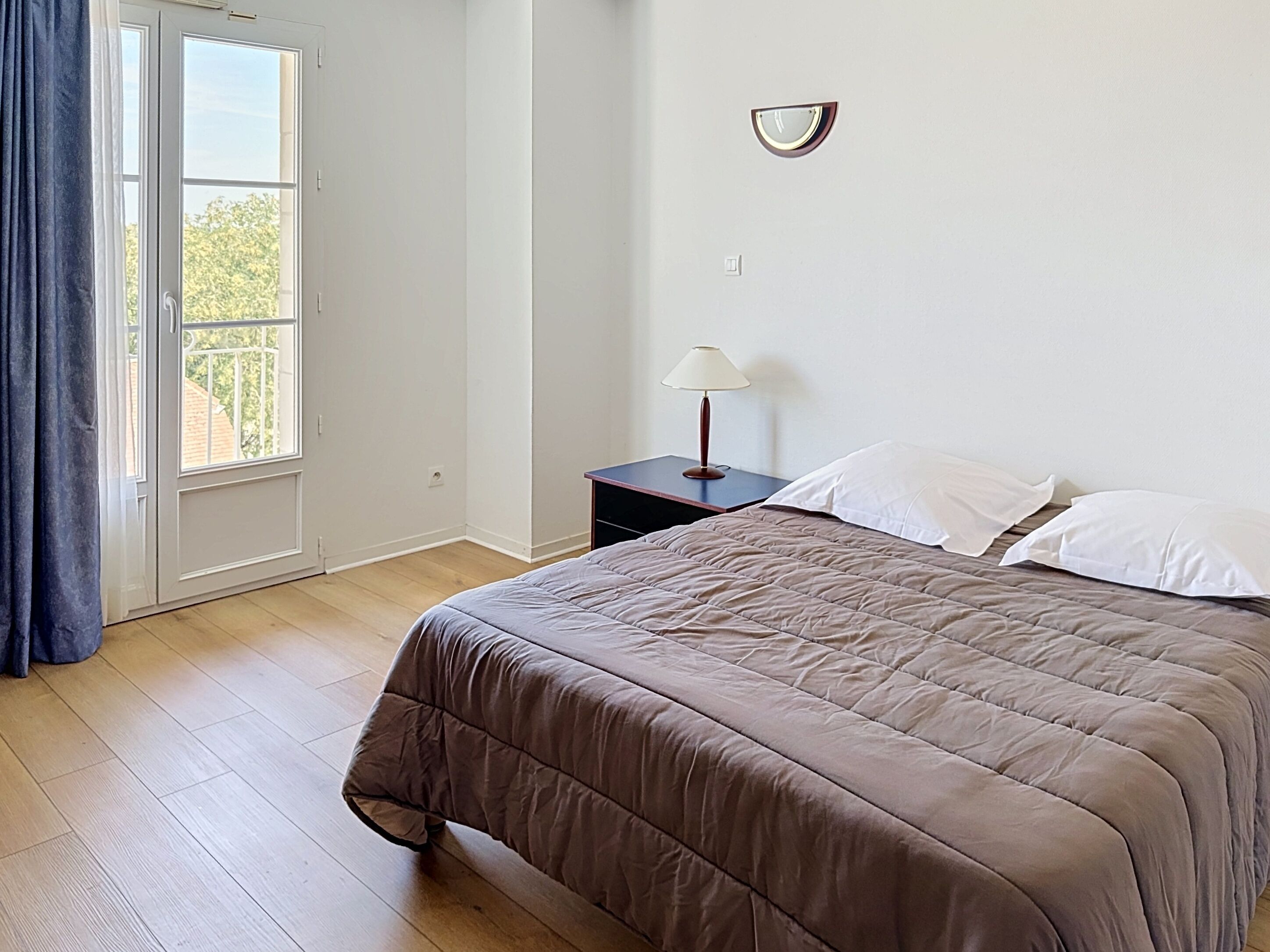 A bedroom with a bed, a nightstand, a lamp, and a window with curtains.
