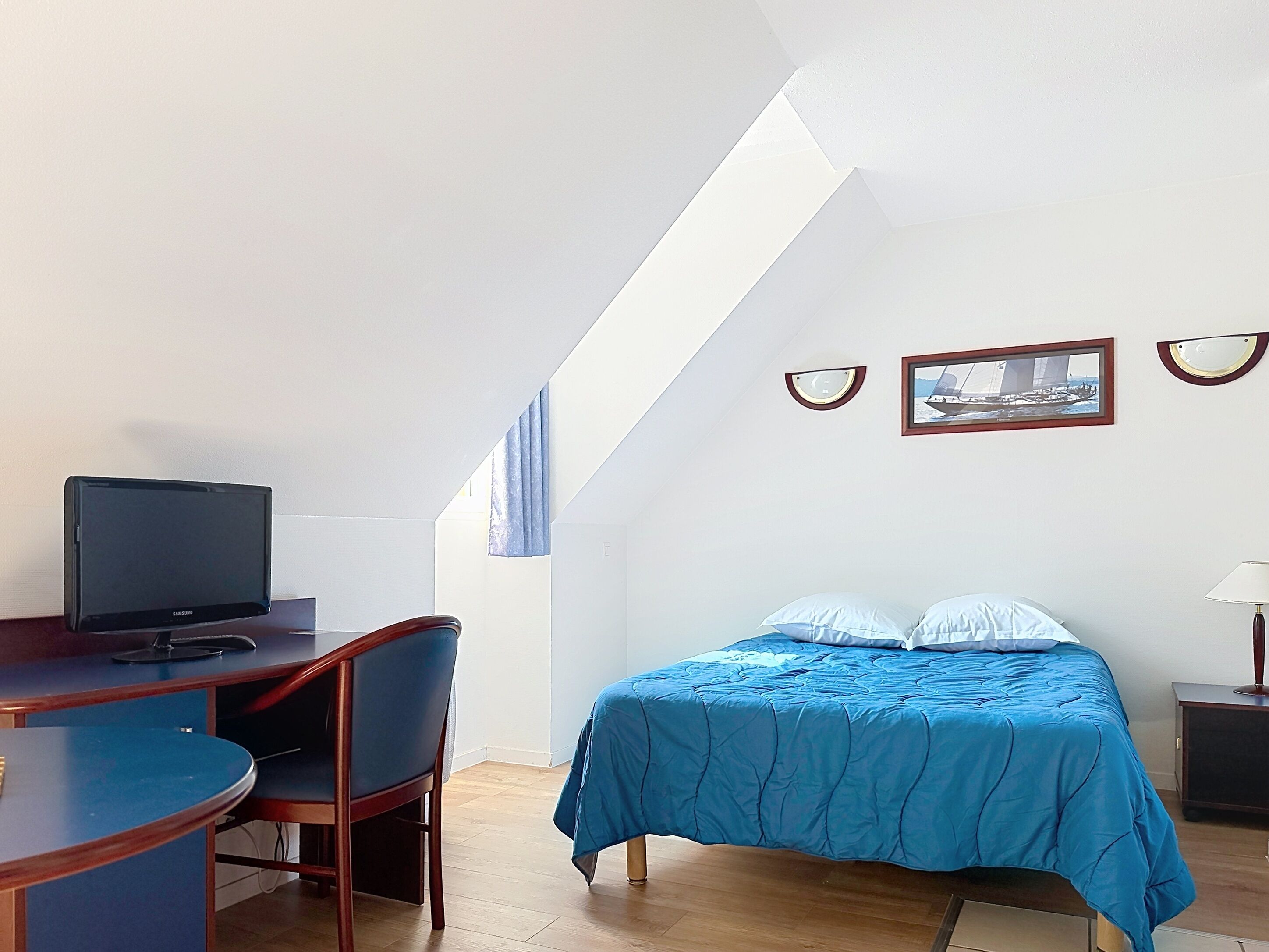 A room with a bed, a desk with a TV, a chair, and a lamp.