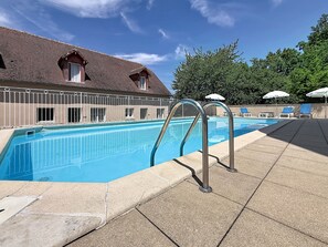 A swimming pool with metal railings, lounge chairs, and umbrellas, surrounded by a building with a tiled roof. - Terres de France - Appart'Hôtel La Roche Posay (La Roche-Posay)