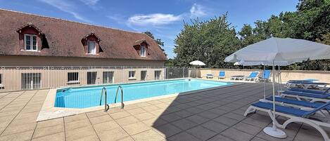 Una piscina con cubierta de azulejos, sillas de descanso y sombrillas.