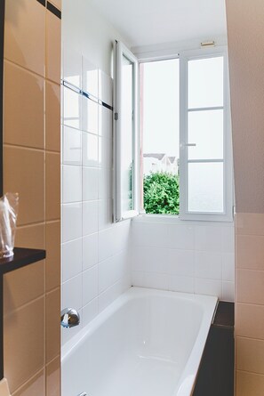 Une salle de bain avec une baignoire, une fenêtre donnant sur un espace verdoyant et un porte-serviettes.