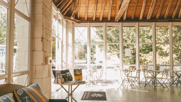 A spacious room with large windows, a wooden ceiling, and a seating area with a sofa and tables. - Terres de France - Appart'Hôtel La Roche Posay (La Roche-Posay)