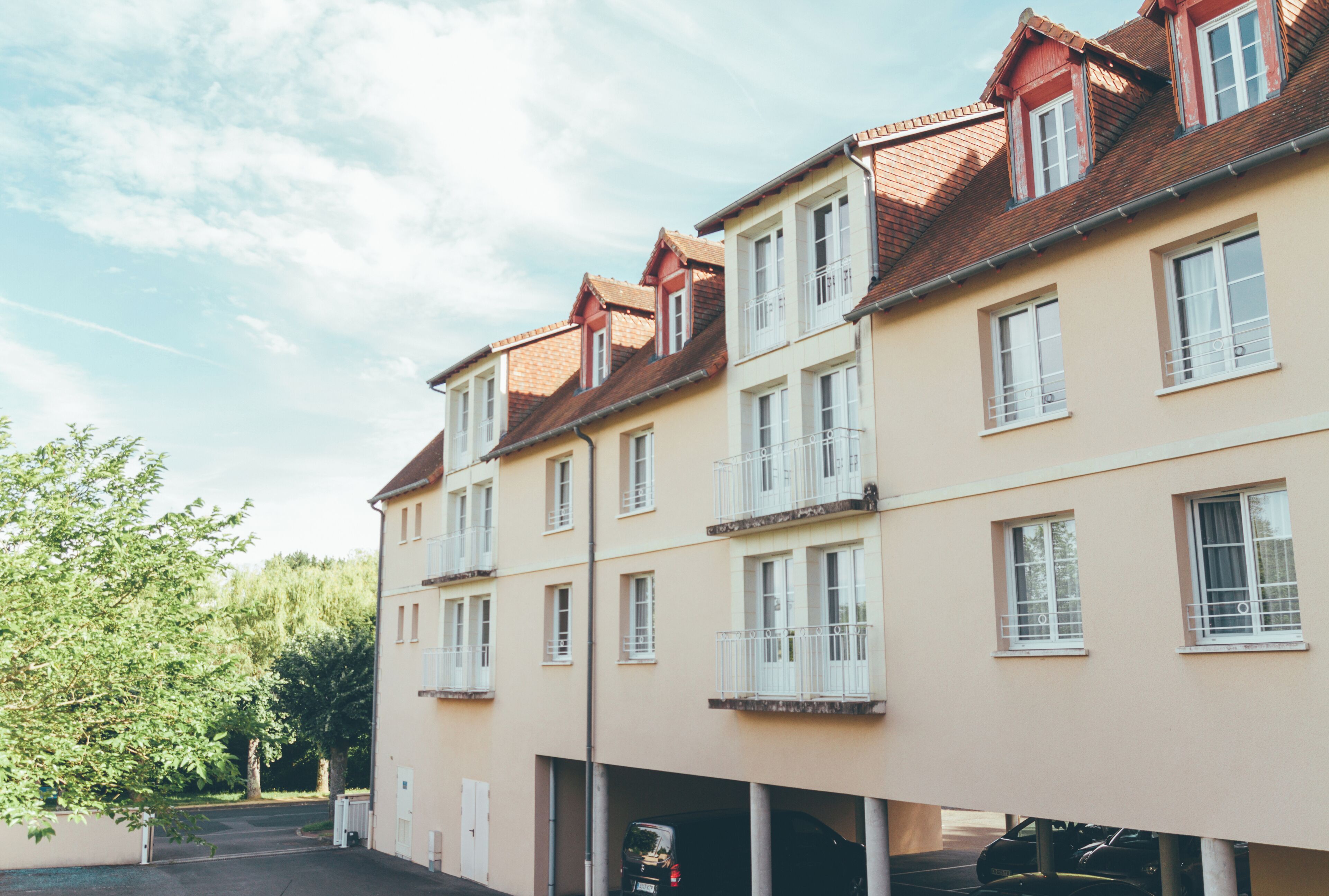 Un edificio residencial de varios pisos con fachada color crema, techos de tejas rojas y ventanas enmarcadas en blanco.