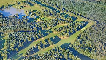 An aerial view of a golf course with multiple greens, a pond, and dense forested areas.