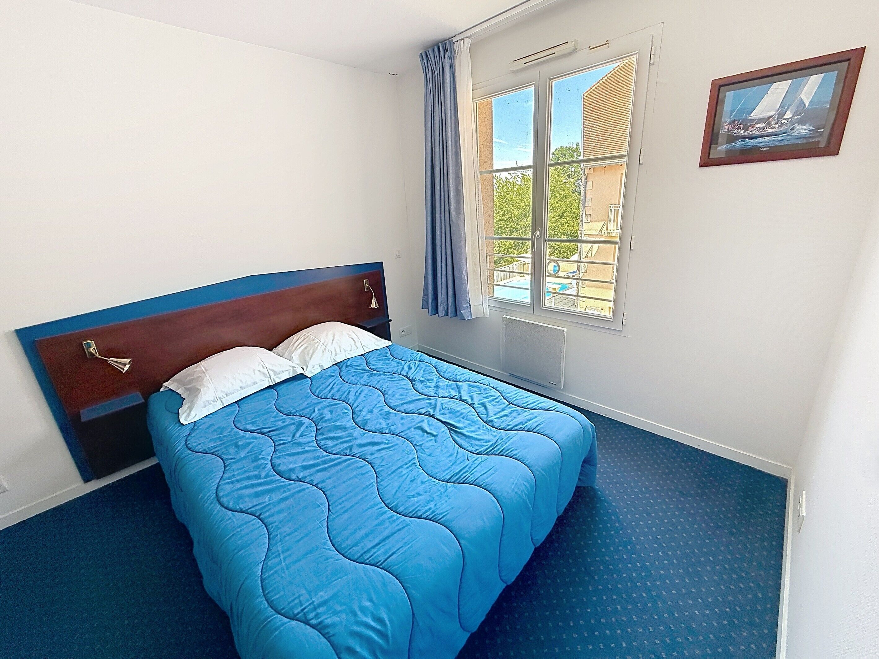 Un dormitorio con cama, ventana con cortinas e imagen enmarcada en la pared.