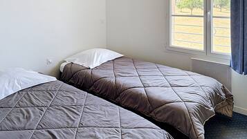 A room with two beds, a window with a view of a field, and a framed picture on the wall.