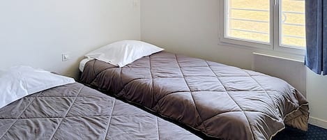 A room with two beds, a window with a view of a field, and a framed picture on the wall.