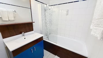A bathroom with a white sink, blue cabinet, and a glass-enclosed shower.