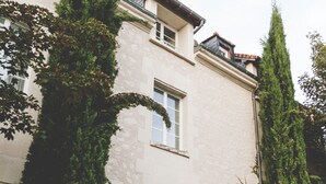 A building with a stone facade, a door with a window, and a small garden area with pink flowers. - Terres de France - Appart'Hôtel La Roche Posay (La Roche-Posay)