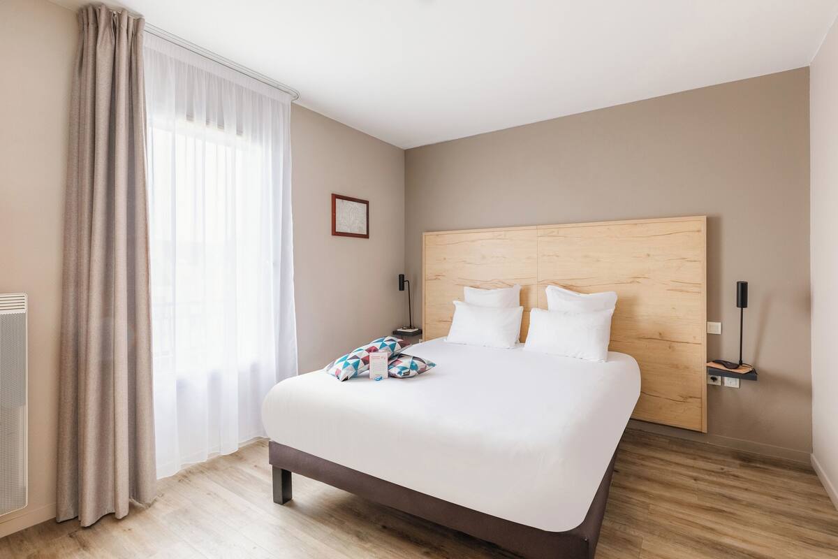 A modern hotel room with a large bed, wooden headboard, and a bedside table with a lamp.