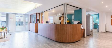 Un espace d’accueil moderne, doté d’un comptoir de réception en bois, d’une cloison en verre et offrant une vue sur les bureaux.