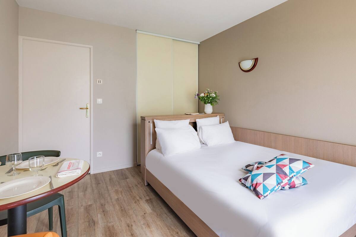 A hotel room with a bed, bedside table, and a small table with a chair.