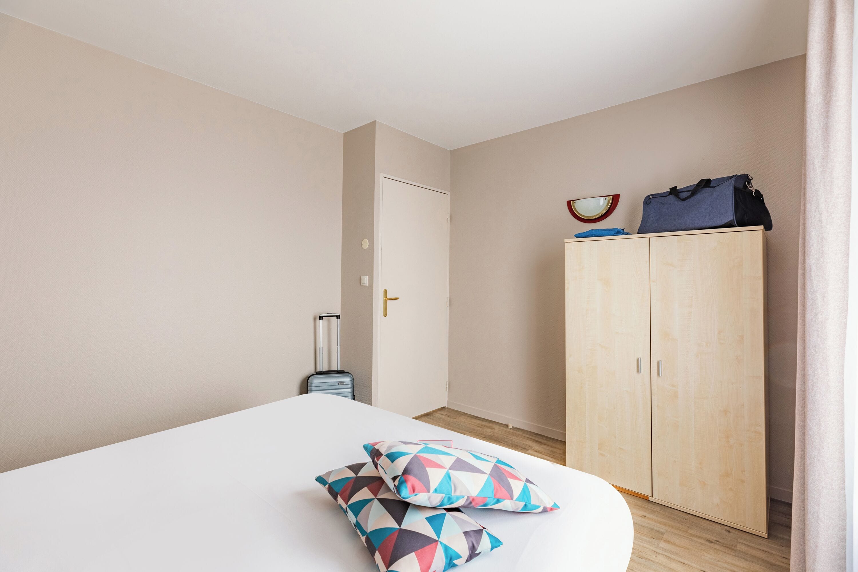 A hotel room with a bed, a wardrobe, and a suitcase.