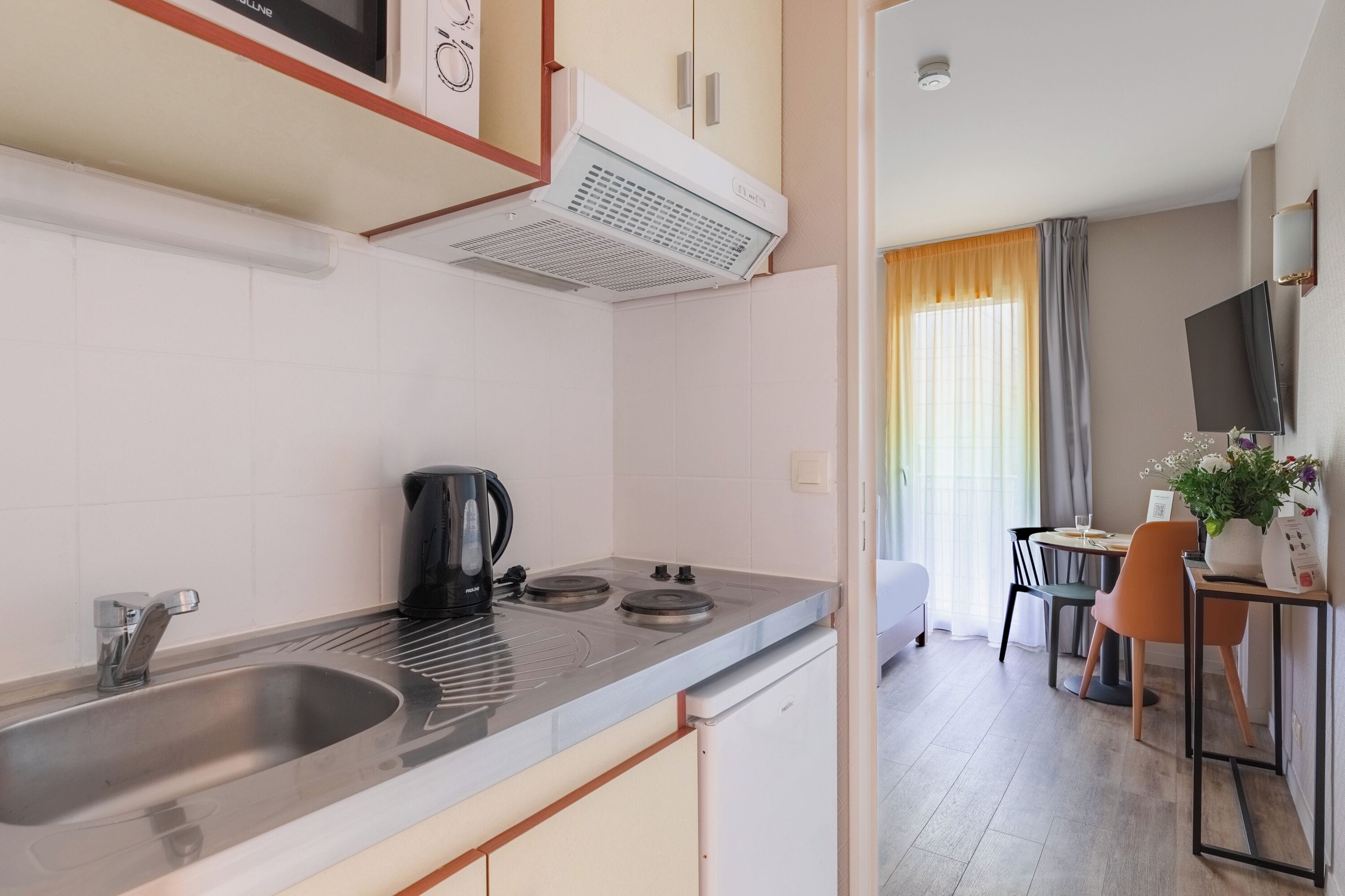 Una cocina moderna con un lavamanos, estufa y hervidor, que da a un comedor con mesa y sillas.