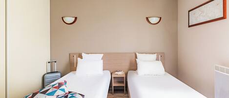 Habitación de hotel con dos camas individuales, una mesita de noche pequeña, una lámpara, una maleta y un cuadro en la pared.