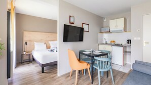 A compact hotel room with a bed, a small dining table with chairs, a TV mounted on the wall, and a kitchenette. - Appart'City Confort Nantes Cité des Congrès (Nantes)