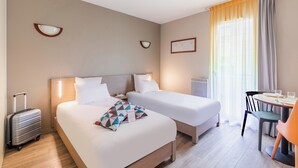 A hotel room with two beds, a desk with a chair, a suitcase, and a window with curtains. - Appart'City Confort Nantes Cité des Congrès (Nantes)