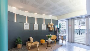 A modern reception area with a grey wall, framed pictures, a wooden chair, a small table, and a potted plant. - Appart'City Confort Nantes Cité des Congrès (Nantes)
