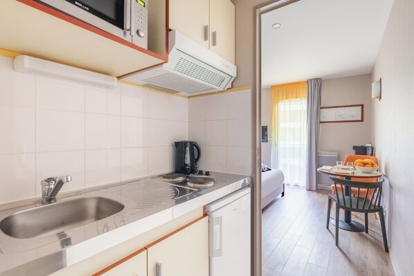A modern kitchen with a microwave, kettle, and sink. There is a dining area with a table and chairs.