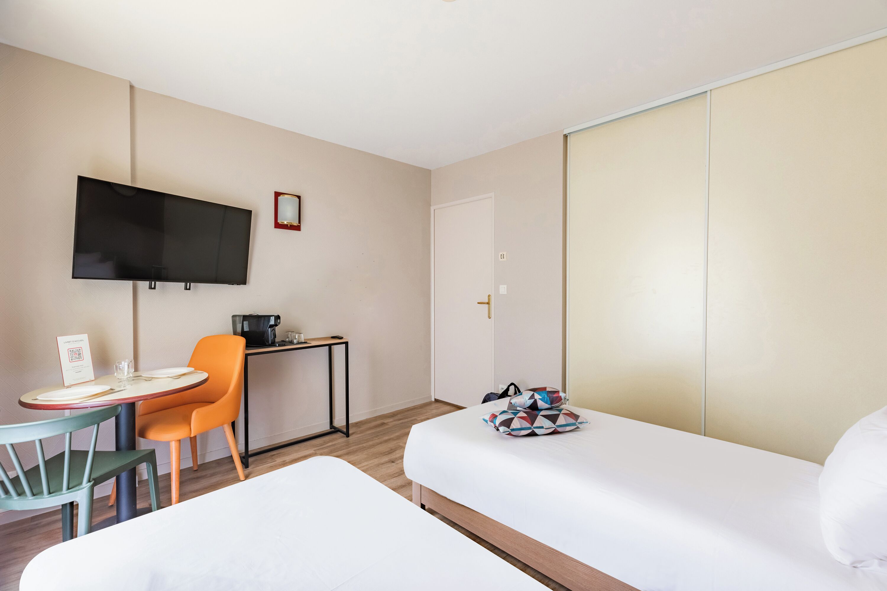 A hotel room with a bed, a desk with a chair, a television, and a wardrobe.