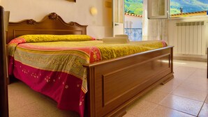 A bedroom with a wooden bed, a painting on the wall, and a view of mountains through the window. - Hotel Villa Fiorentina (Casamicciola Terme)