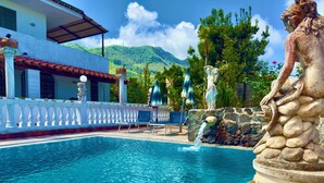 A swimming pool with a stone sculpture, lounge chairs, and a view of a mountain. - Hotel Villa Fiorentina (Casamicciola Terme)