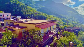A yellow building with a red roof, surrounded by lush greenery and mountains in the background. - Hotel Villa Fiorentina (Casamicciola Terme)