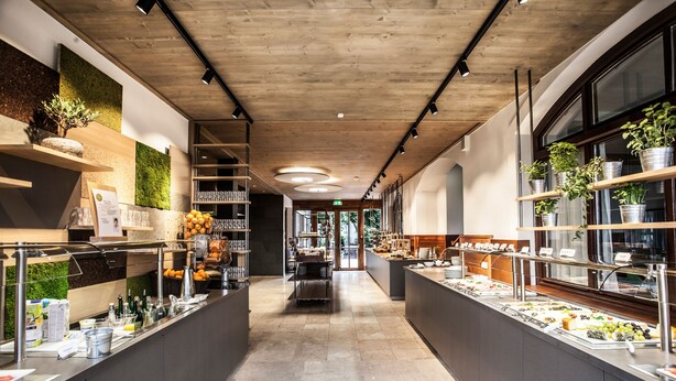 A modern buffet setup with multiple food stations, a wooden ceiling, and potted plants. - Die Wasnerin G'sund & Natur Hotel (Bad Aussee)